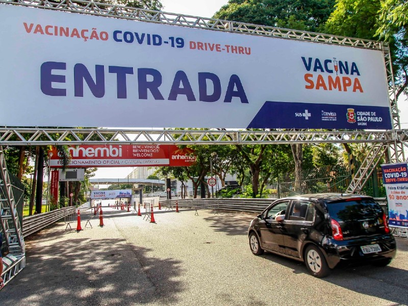 Uma grande faixa indica a entrada do drive-thru do Anhembi. Um carro preto passa por baixo em direção às cabines